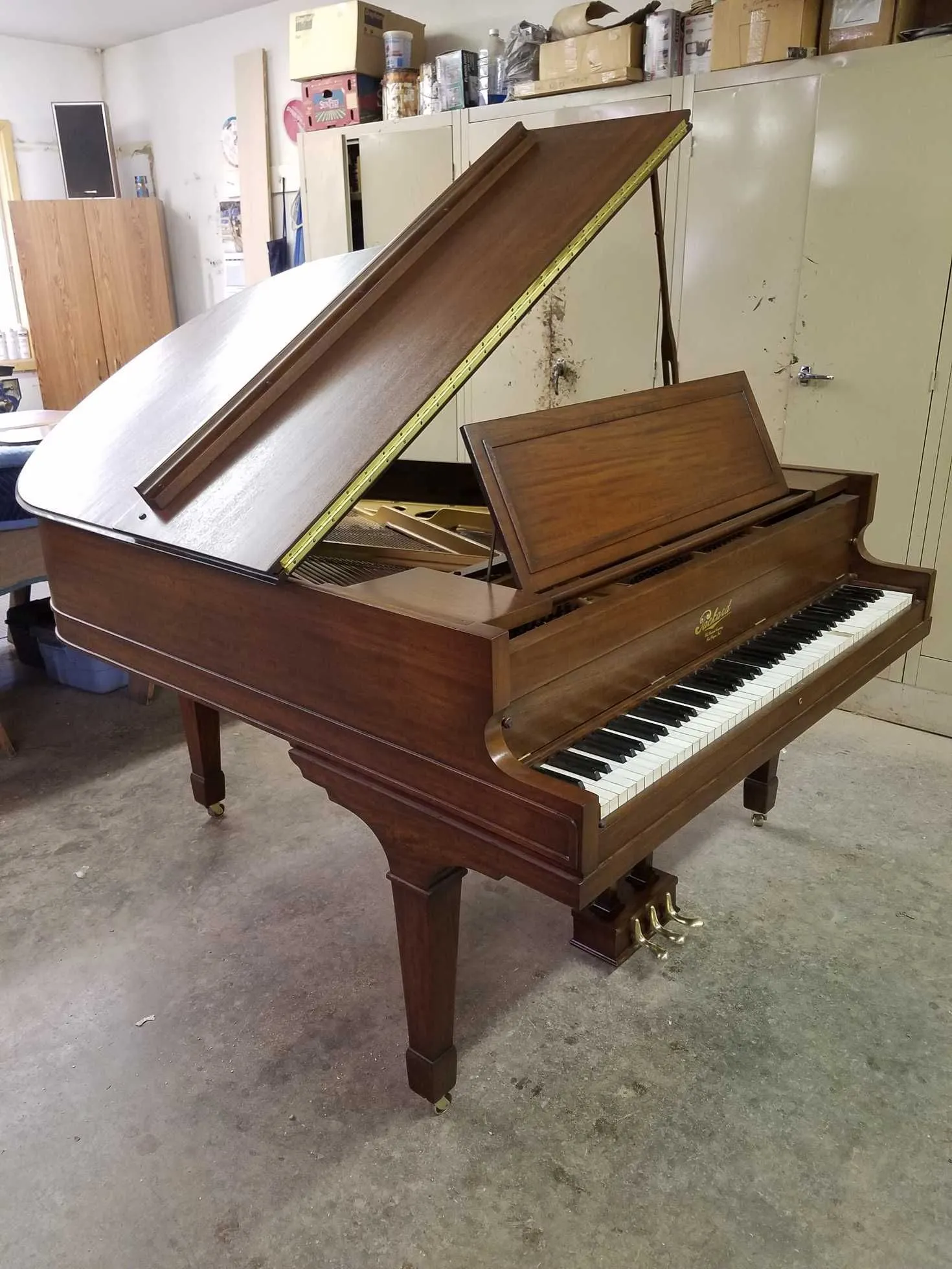 Grand piano, brown wood, open lid, white and black keys, in a room.