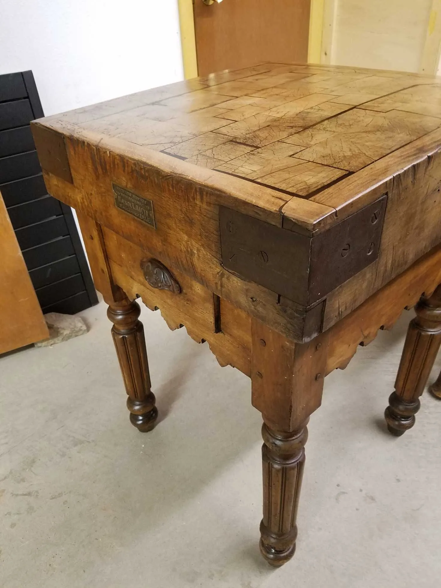 Wooden butcher block table with dark wood legs and metal corner reinforcements in a room.
