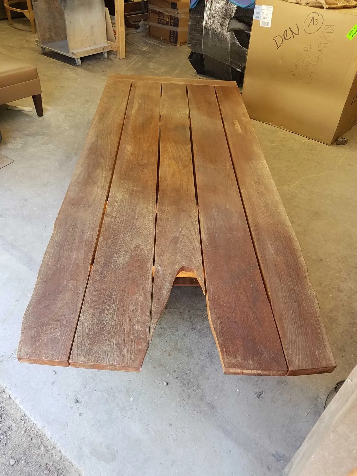 Wooden outdoor picnic table with an A-shaped design, brown and weathered in a workshop setting.