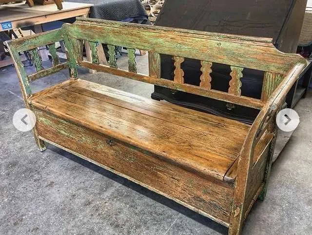 Wooden bench with distressed green and brown paint. Interior with back and armrests, and storage.